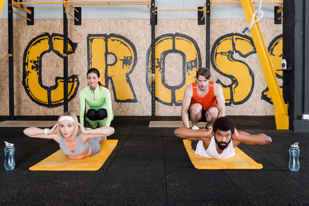 young trainers assisting interracial sports people doing abs exercise in gym - Photo, Image