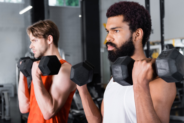bearded african american man training with dumbbells near blurred friend - Photo, Image