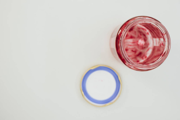 A top view of an open empty strawberry jam jar with lid isolated on light gray background - Fotó, kép