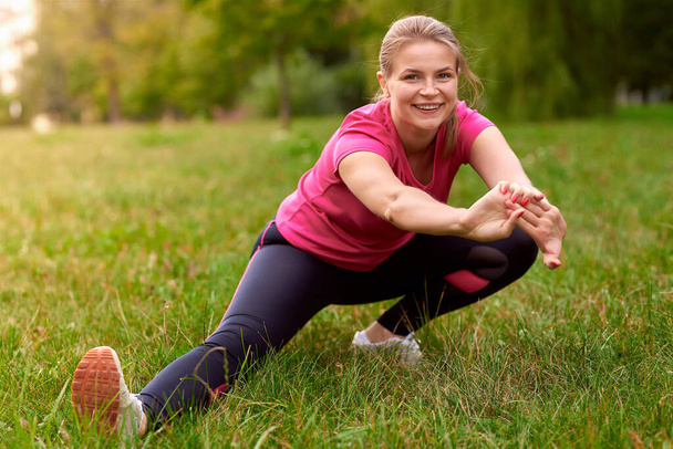 молодая женщина в спортивной одежде делает выпады, растягиваясь в парке фитнес-тренировки на открытом воздухе - Фото, изображение