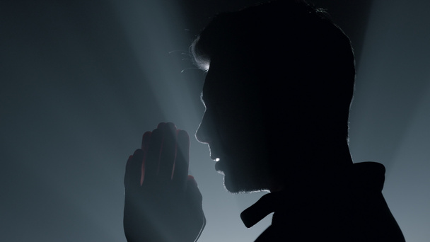 Silueta hombre rezando en la oscuridad. Hombre susurrando oración en el interior. - Foto, imagen