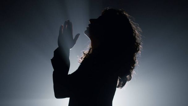 Silhouette Frau betet in der Dunkelheit. Gläubige Mädchen flüstern Gebet im Haus. - Foto, Bild