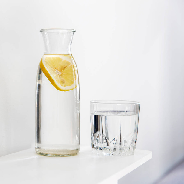 Ferahlatıcı bir bardak su, içinde bir dilim limon olan bir şişe yaz sıcağında şifoniyerin üzerindedir. Kare kare - Fotoğraf, Görsel