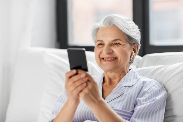 senior woman with smartphone and earphones in bed - Foto, Imagem