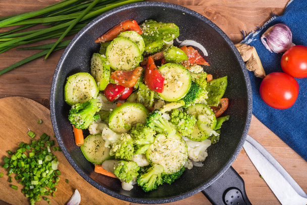 Vegetáriánus brokkoli, cukkini, hagyma és paradicsom serpenyőben. A zöldségeket egy wokban párolják. Sütő serpenyő zöldségekkel az asztalon, felülnézet - Fotó, kép