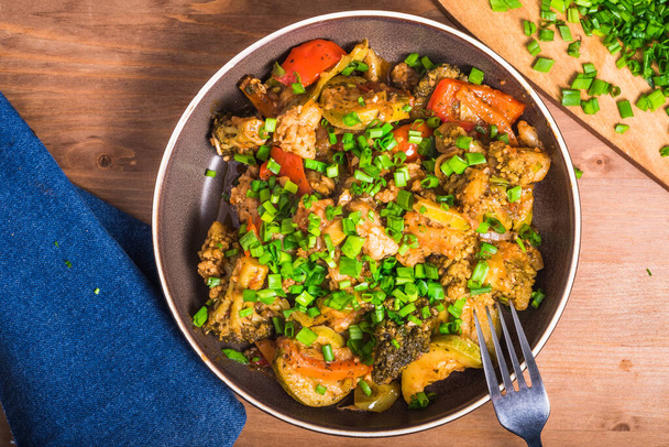 Plato vegetariano de brócoli, calabacín, cebolla y tomate en un plato, vista superior. Servir estofado de verduras en un plato con cebolletas. - Foto, imagen