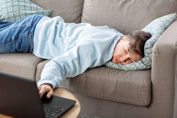 bored man with laptop lying on sofa at home - Photo, Image