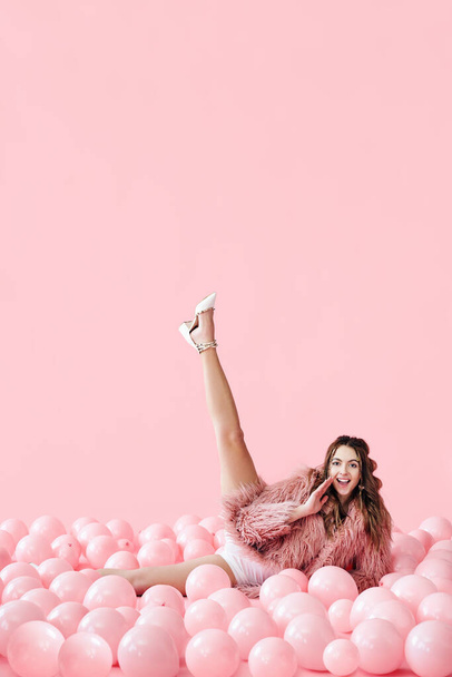 Funny smiling woman lying in many pink balloons with her legs up - Fotó, kép
