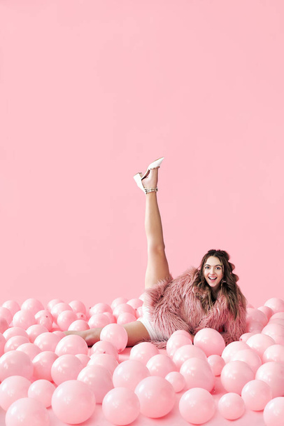 Funny smiling woman lying in many pink balloons with her legs up - Photo, Image