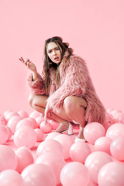 Displeased hipster woman sitting in many pink balloons background - Valokuva, kuva
