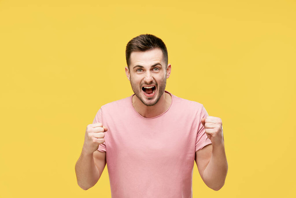 Young man celebrating with winner gesture on yellow background - Fotografie, Obrázek