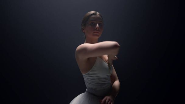 Tender baletnica patrząc aparat w ciemnym tle. Lekcja tańca baletowego - Zdjęcie, obraz