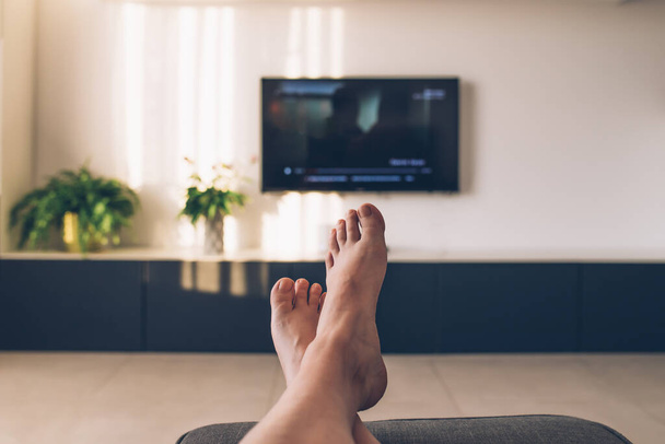 Selective focus image of relaxing feet and tv in a modern living room with natural sunset lights.  - Φωτογραφία, εικόνα