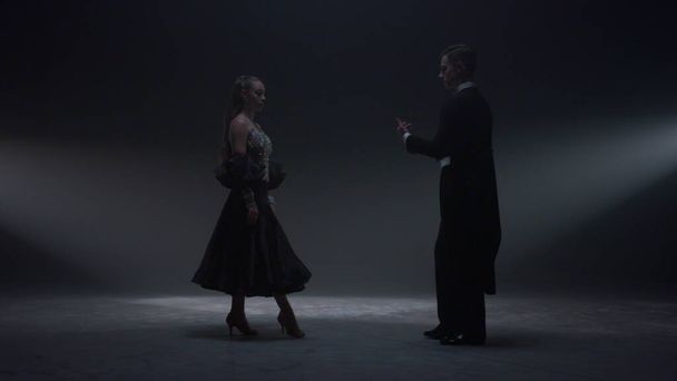 Danskoppel houdt elkaars hand op het donkere podium. Man nodigt vrouw uit om binnen te dansen. - Foto, afbeelding