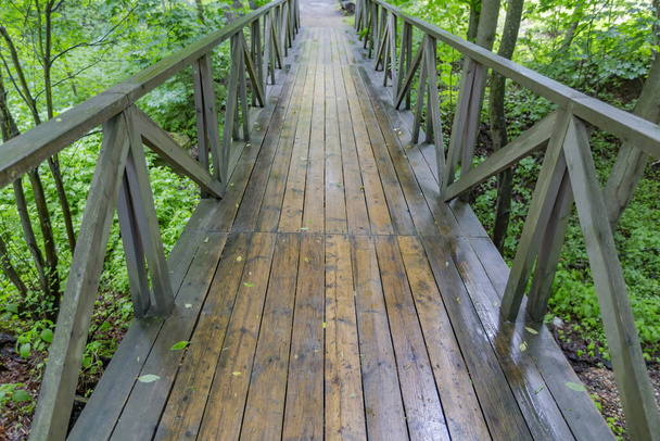 Un pequeño puente hecho de tablas de madera con pasamanos a través de un estrecho arroyo en un parque de la ciudad - Foto, imagen