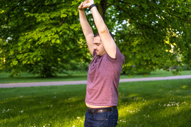 Foto di un giovane e attraente uomo nel parco che stringe le braccia verso il cielo e gli occhi chiusi. Da solo nella natura durante una giornata estiva. Posizione yoga - Foto, immagini
