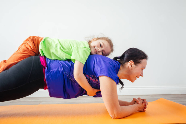 Active boy laying on his mother while she is standing in plank - Foto, Bild
