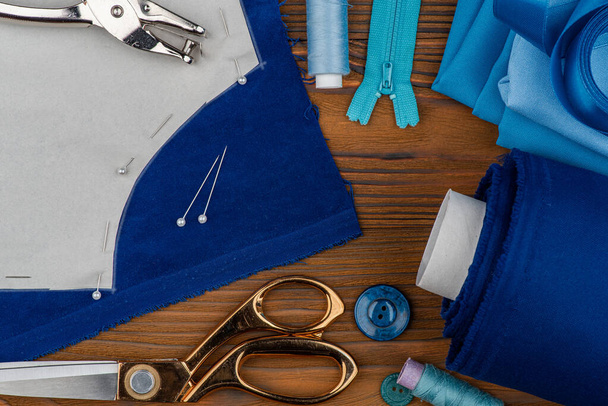 カスタマイズされた衣類、縫製アクセサリーをカットして縫います。はさみ、糸、縫製パターン、木製のテーブルの上の青い生地. - 写真・画像