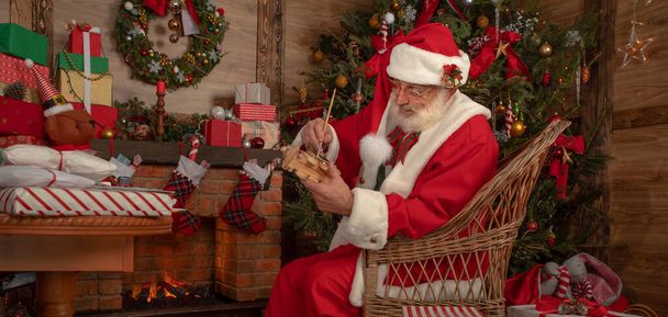 Mikulás, hogy játékok a műhelyben ünnepi belső fából készült ház, Szilveszter vidám hangulata Spirit of Christmas. Idős férfi igazi fehér szakáll cosplay Mikulás Karácsony. - Fotó, kép
