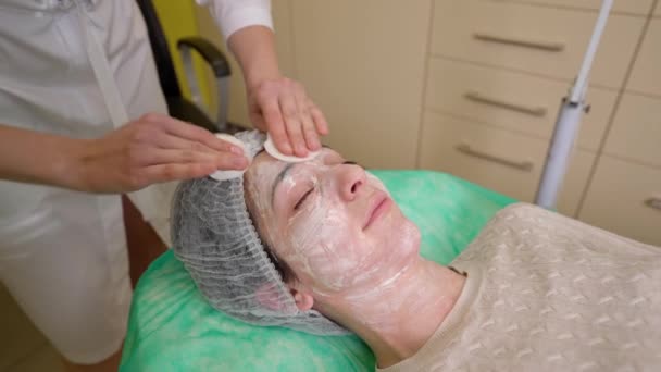 Vrouwelijke schoonmaakster schoonmaken gezicht van jonge vrouw van cosmetische masker - Video