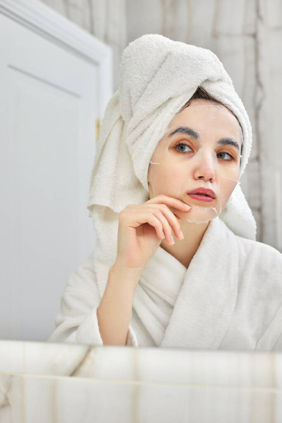 woman in white bathrobe in front of mirror in bathroom - Fotó, kép