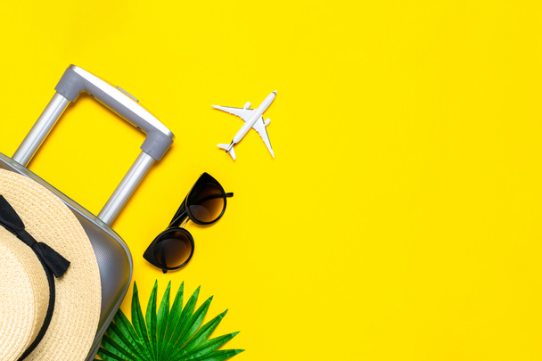 Zomer achtergrond strand. Koffer, zonnebril met palmblad en strohoed, wit vliegtuig in reissamenstelling op gele achtergrond. Rustige strand scene met kopieerruimte - Foto, afbeelding