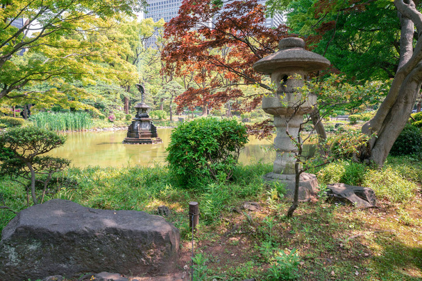 Tokio, Japan - 12.05.2019: Steenlantaarn, kraanstandbeeld fontein en kleurrijke bomen van Hibiya park in het centrum - Foto, afbeelding