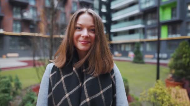 Portrait of a gorgeous dark haired woman smiling charmingly while standing against the background of modern buildings. Happy young woman enjoys life. Slow motion - Footage, Video