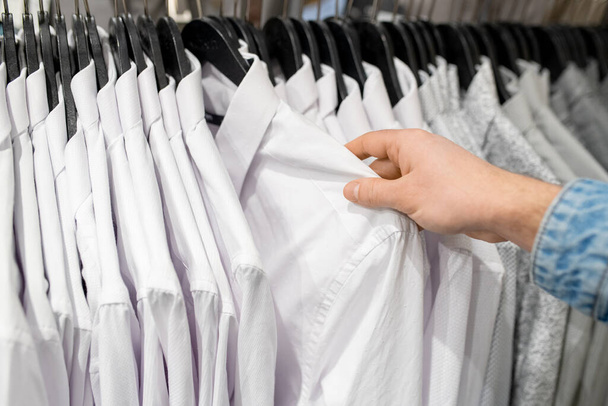 A vásárló keze fehér inget választ a ruhaboltban. - Fotó, kép