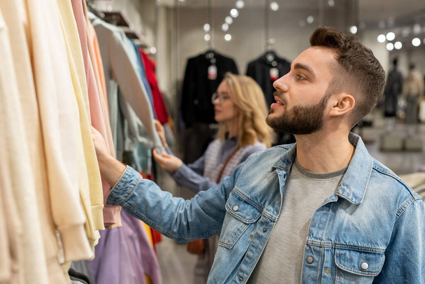 Een man en vrouw op zoek naar trendy kleding in de hedendaagse winkel - Foto, afbeelding