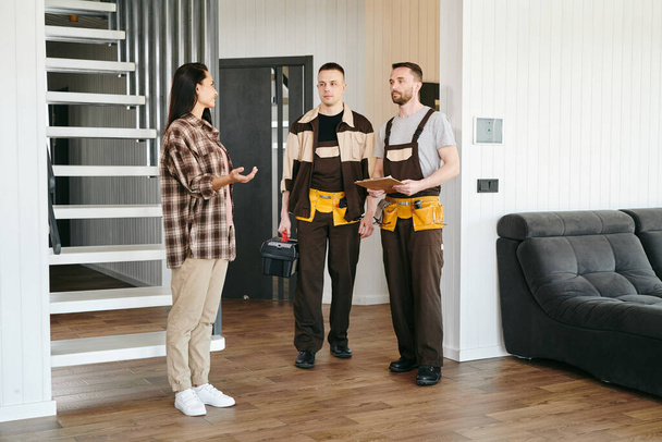 Two plumbers and young female having conversation about plumbing problems in living-room - Foto, afbeelding