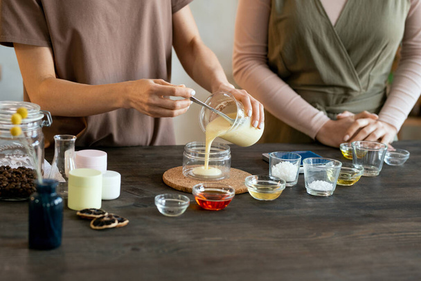 Young female putting blob of fresh handmade liquid soap mass on palm of her friend helping her with making natural handmade cosmetic products - Photo, Image