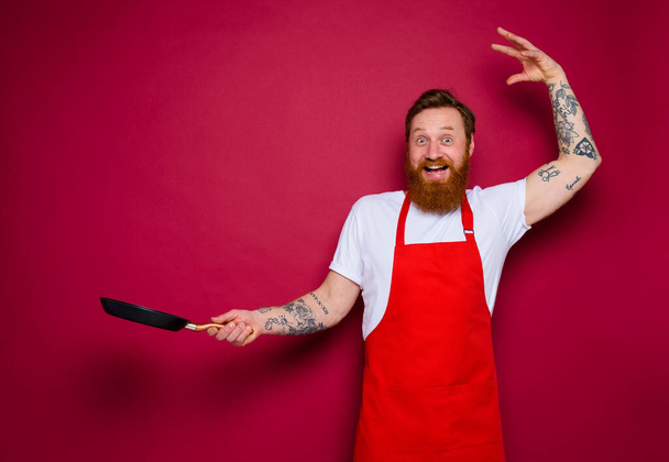Chef feliz con barba y delantal rojo cocineros con sartén - Foto, imagen