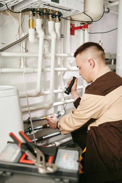 Mladý opravář v uniformě opravy potrubí v záchodě velkého domu - Fotografie, Obrázek