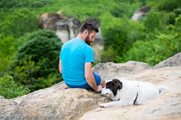 hombre con su perro sentado en una roca disfrutando de la naturaleza - Foto, imagen