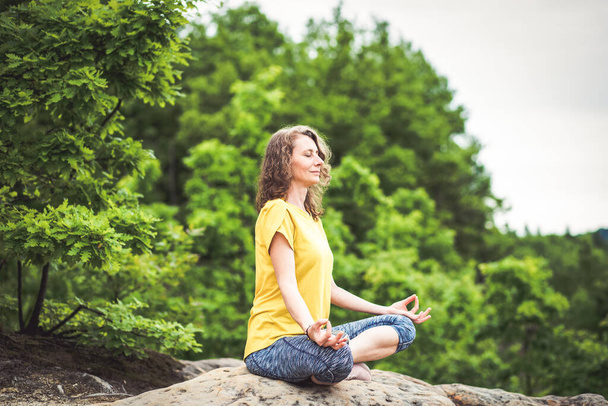 woman meditating in lotus pose on a rock in summer - Zdjęcie, obraz