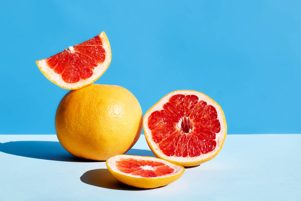 Fresh healthy grapefruit on sunlight with hard shadows. Minimal food creative concept on blue pastel background. Grapefruit slices citrus fruits. - Photo, Image