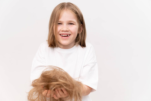 Szczęśliwa dziewczynka trzyma w rękach przycięte włosy po cięciu na białym tle. oznacza dbać o włosy dzieci. Salon piękności dla dzieci. - Zdjęcie, obraz