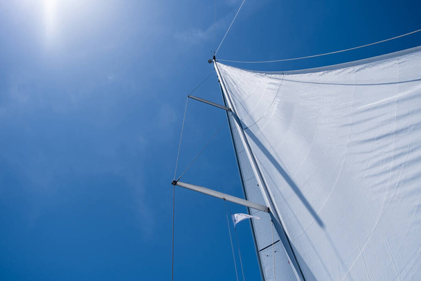 Sailing with the wind at open sea ocean, summer holidays concept. Yacht wind filled sails on clear blue sky background. Looking up at the sky, sun shining, sunbeams on boat rigging, Low angle view - Foto, immagini