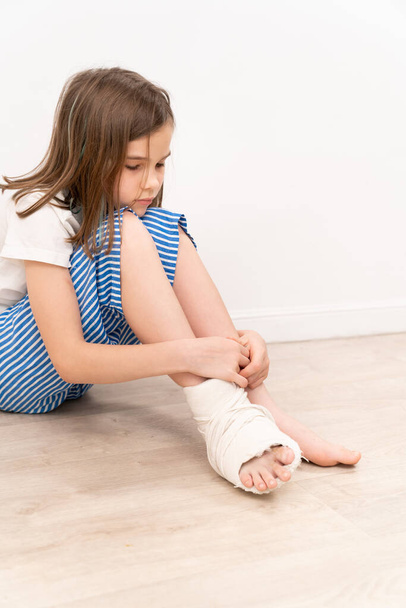 Triste adolescente con yeso ortopédico en su pie sentado en el suelo. cirugía para corregir la deformidad del pie en niños. pacientes pequeños y móviles. - Foto, Imagen