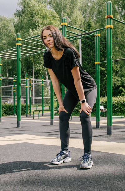 a girl in a black T-shirt and leggings holds her hands on her hips and goes in for sports - Fotoğraf, Görsel