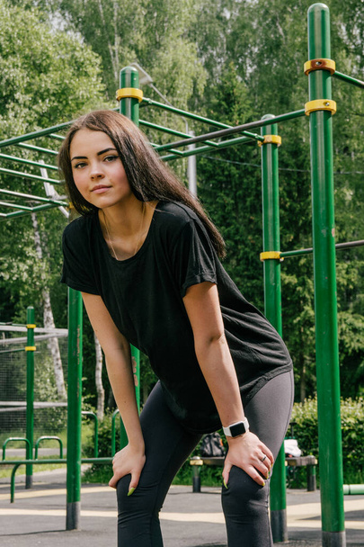 a girl in a black T-shirt and leggings holds her hands on her hi - Valokuva, kuva