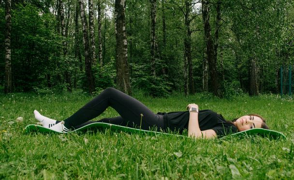 a girl in a black T-shirt and leggings lies on a sports mat and  - Fotografie, Obrázek