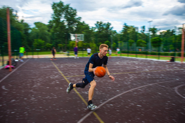 Fiatal vörös srác fut és csöpög a kosárlabda nagy sebességgel egy sportpályán az utcán a nap folyamán mozgás elmosódott - Fotó, kép