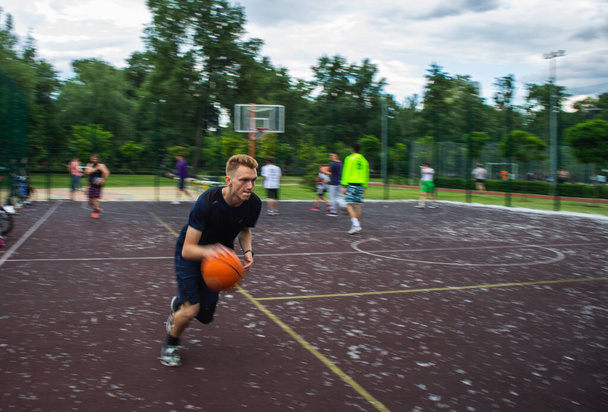 日中の動きがぼやけている間、若い赤毛の男は通りのスポーツ場で高速でバスケットボールを走らせ、ドリブル - 写真・画像