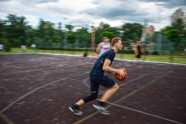 Nuori punapää kaveri käynnissä ja dribbling koripallo suurella nopeudella urheilukentällä kadulla päivän aikana liike hämärtynyt - Valokuva, kuva
