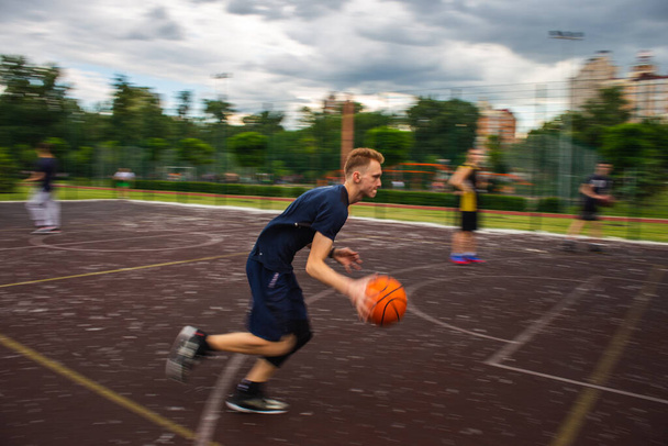 Joven pelirrojo corriendo y goteando una pelota de baloncesto a alta velocidad en un campo de deportes en la calle durante el día movimiento borroso - Foto, Imagen