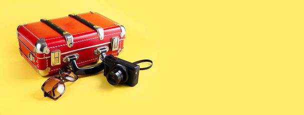 Czerwona walizka podróżna, okulary przeciwsłoneczne i kamera na żółtym tle. Koncepcja podróży. Sztandar. Miejsce na SMS-a. Wysokiej jakości zdjęcie - Zdjęcie, obraz