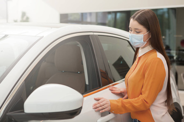 Woman wearing medical face mask, choosing new car to buy during covid-19 pandemic - Фото, изображение