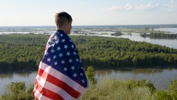Blonďatý chlapec mává národní vlajkou USA venku nad modrou oblohou na břehu řeky - Záběry, video